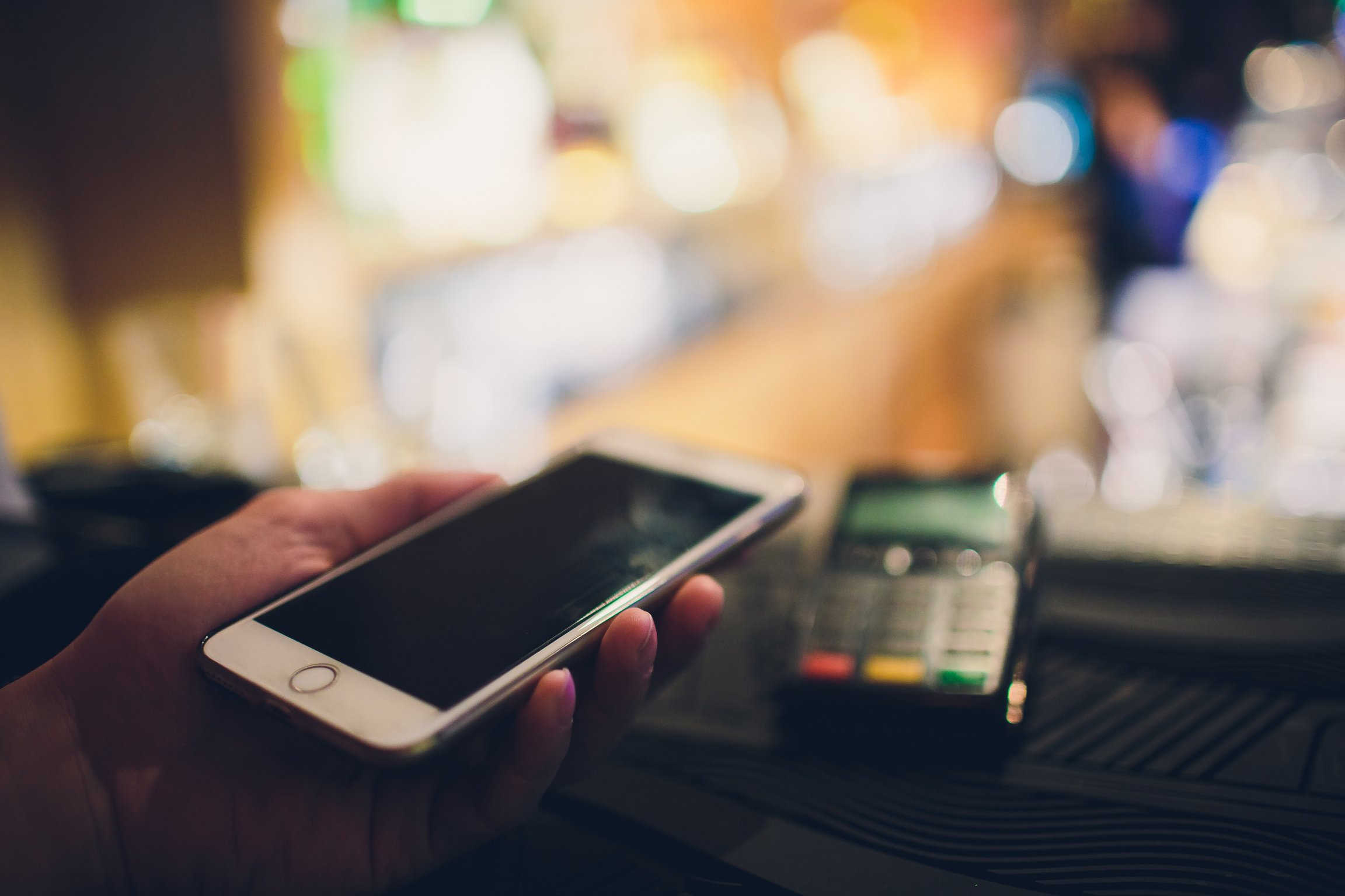 Closeup of a customer using her bank card and nfs technology to pay a barista for her purchase at a cafe.